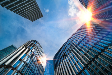 Modern high-rise buildings bottom view and sun shining on blue sky. Top parts of skyscrapers in...