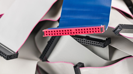 Blue parallel multi wire ribbon cable with pink connector on pile of white flat cords. Detail of...