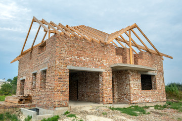 Building site with unfinished brick house with wooden roofing frame for future roof under...