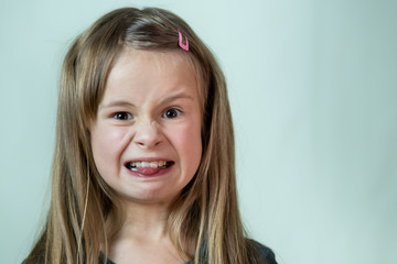 Close-up portrait of little girl with long hair making disgust expression.