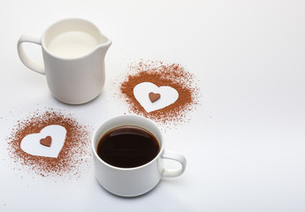 Two shapes of heart from cacao powder, cup of coffee with milk and copy space on white background.