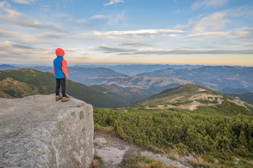 Young child boy hiker standing in mountains enjoying view of amazing mountain landscape.