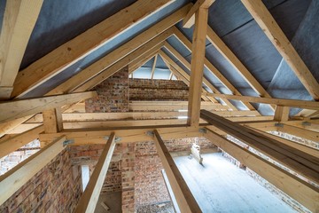 Attic space of a building under construction with wooden beams of a roof structure and brick walls....