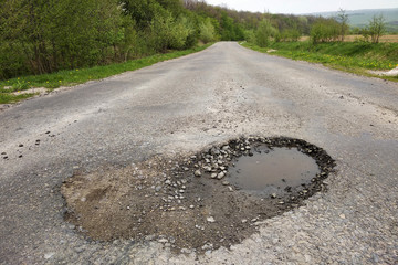 Close up of big pothole with dirty rain water of the road.