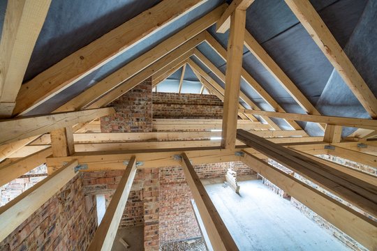 Attic space of a building under construction with wooden beams of a roof structure and brick walls. Real estate development concept.