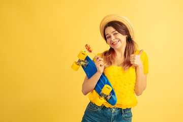 Dreamful, holds skate. Caucasian woman's portrait on yellow studio background. Beautiful female model in hat. Concept of human emotions, facial expression, sales, ad. Summertime, travel, resort.