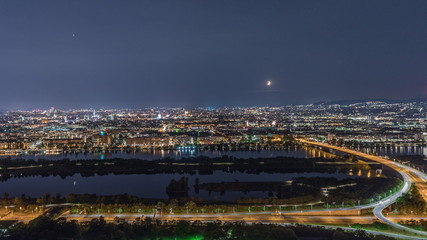 Naklejka premium Aerial panoramic view over Vienna city with skyscrapers, historic buildings and a riverside promenade night timelapse in Austria.