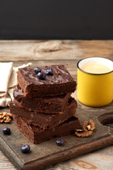 stack of square baked slices of brownie chocolate cake with walnuts on a wooden surface