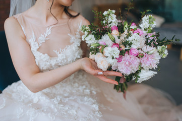 The bride in a white dress holds a wedding bouquet of roses in her hands. Closeup portrait of fresh...
