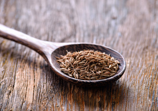 Cumin seeds in spoon on wooden table