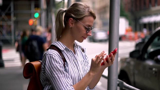 Positive hipster girl in spectacles taking pictures of showplaces via application on modern cellphone during chatting with followers from web blog connected to 4g wireless for communicate