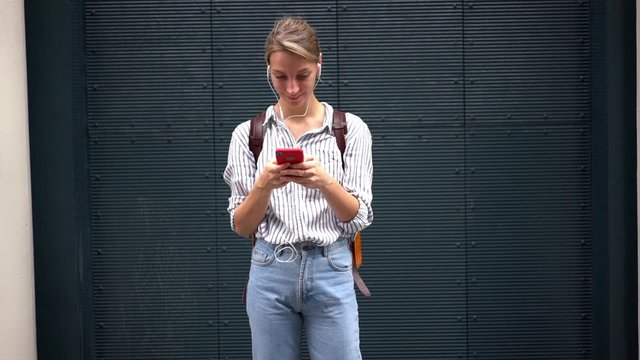 Slow motion effect of attractive hipster girl enjoying favorite songs in modern headphones, female tourist listening music and chatting with followers from social networks via phone device