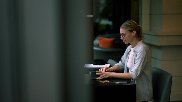 Serious female remote worker typing report on laptop computer analyzing information rereading text from laptop, woman in eyewear making booking online on organizing job connected to wifi