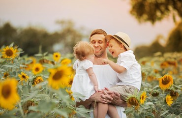A happy family walks in a field of sunflowers. Young handsome dad with two children in a sunflower field.