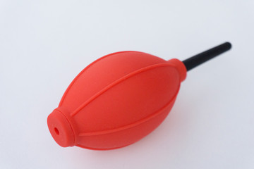 Red and black camera air blower for clearing dust particles from lens.