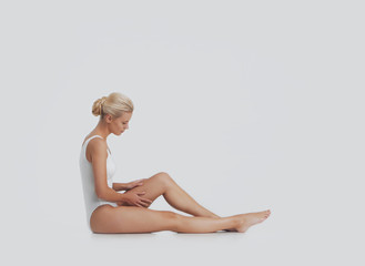 Fototapeta premium Young, beautiful, fit and natural blond woman in white swimsuit applying moisturizing cream. Massage, skin care, cellulite removal, sport and weight loss.
