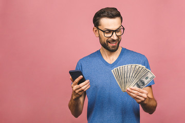 Excited man in casual t-shirt holding lots of money in dollar currencys and cell phone in hands...