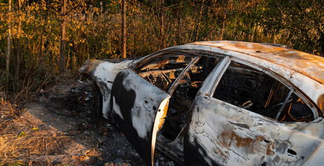 Burnt out, Wrecked car after an explosion or fire. Rusty, burnt car interior with ash, molten glass and metal parts. Abandoned car in the forest near the city. The concept of a traffic accident. 