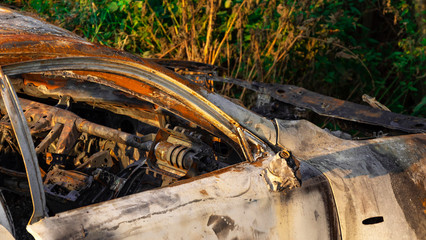 Burnt out, Wrecked car after an explosion or fire. Rusty, burnt car interior with ash, molten glass and metal parts. Abandoned car in the forest near the city. The concept of a traffic accident. 