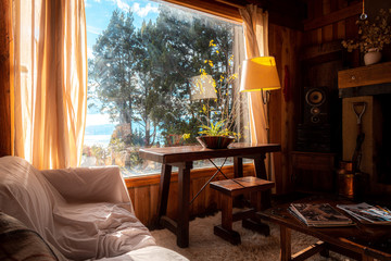 BARILOCHE, ARGENTINA, JUNE 18, 2019: Interior of a cozy and relaxing cabin with comfortable couches around the fireplace, illuminated by the sunlight from the window that sees to the forest and lake.
