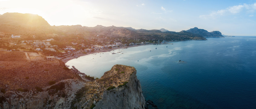 Aerial view of beautiful grand beach in Stegna on Rhodes island at sunset. Tourists under umbrella chill relax near clear blue emerald turquoise sea water.