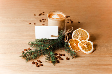 Composition of a cup of latte, coffee beans, dried oranges and a fir branch 