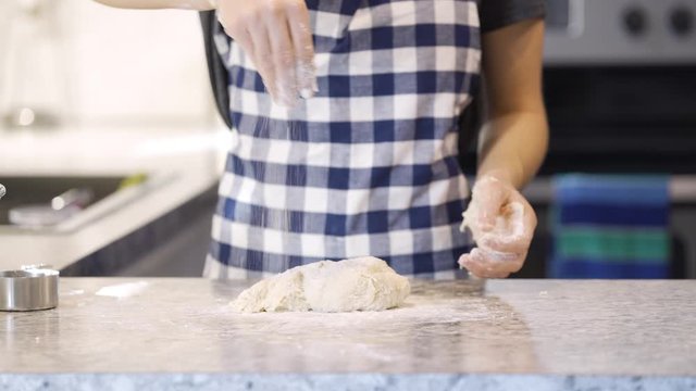 Woman preparing dough for baking bread and kneading the dough on counter while adding ingredients