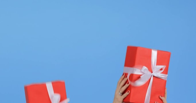 The hands of young girls throw up fun boxes on a blue background. Christmas gifts decorated with a white ribbon appear on a blue background.