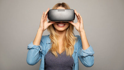 A technophile girl. Close up photo of a happy woman in VR glasses, who is holding them with her hands, facing the camera.