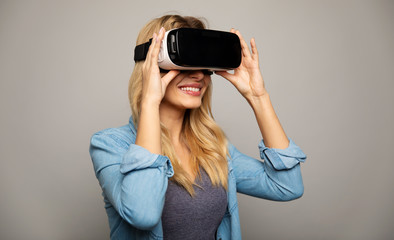 Futuristic games. Close up photo of a smiley blonde woman in VR glasses, who is touching them with...