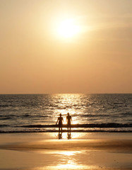 Fototapeta na wymiar Silhouette of an unrecognizable young couple standing together on a golden beach looking towards a setting sun