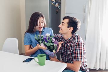 Man gifting bouquet of flowers to his girlfriend on kitchen at home. Valentines day romantic surprise