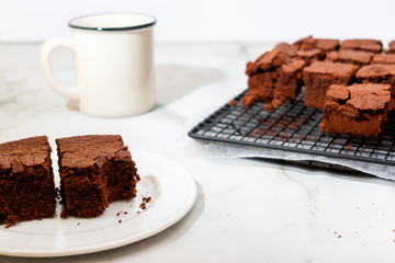 Close view of homemade stacked brownies on a plate and over cooling rack with a mug over marbled background with copy space. High key 