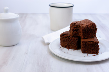 Close view of homemade stacked brownies with mug and pot over wooden background with copy space. High key 