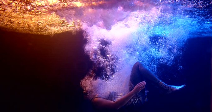 woman in a silver dress with long red hair falls under the water as if into another dimension