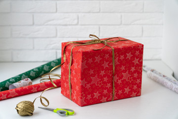 Bright red gift box with golden ribbon in front of white brick wall and colorful gift wrapping...