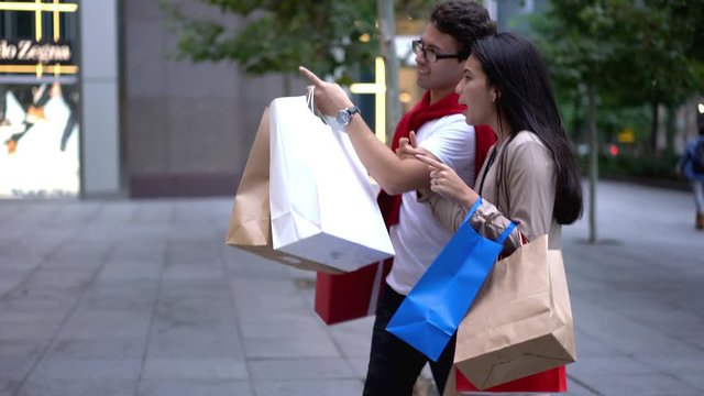 Cheerful Latino American Couple In Love Spending Time For Shopping Gifts And Presents For Family Walking Around Downtown With Paper Bags In Hands And Searching Stores During Leisure Time