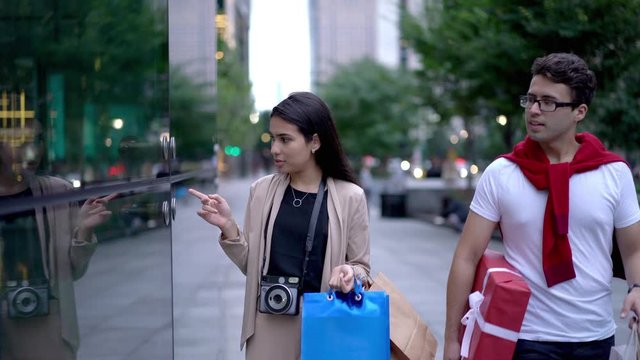 Attractive latino american hipster girl with old fashioned camera on neck walking around downtown and talking with boyfriend about relationship, spanish couple enjoying time for shopping