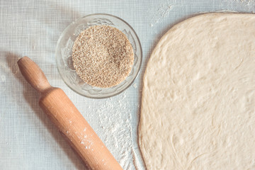 Dough roller and raw dough, pastry ready for pizza with bowl with sesame seeds