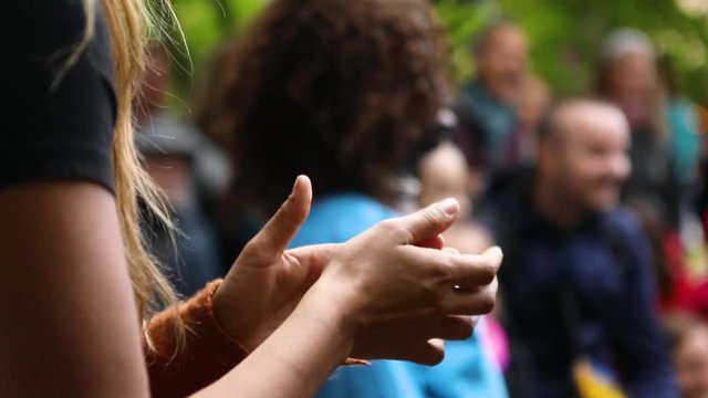 Close up footage of a woman clapping her hands to upbeat music during a festival celebrating Native American music and culture, with blurry people in background