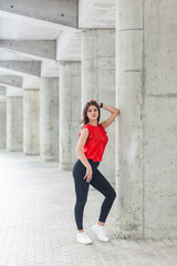 Fototapeta na wymiar beautiful woman in red blouse and jeans posing while leaning on gray column. outdoor shot.