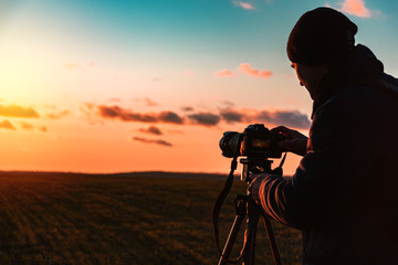 photographer with a tripod and camera takes a landscape during sunset in a large open area