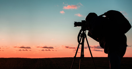 photographer with a tripod and camera takes a landscape during sunset in a large open area
