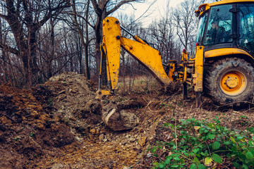 A yellow excavator works on the forest clearing and digs soil.