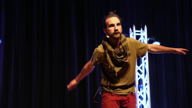 An eager storyteller is seen on stage, flowing arm movements describe legendary and historic tales of Native American culture at spoken word event