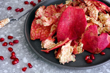 Plate with pomegranate peels on kitchen table with knife and some pomegranate seeds