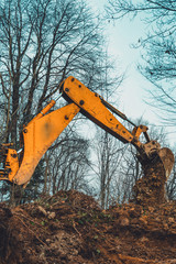 A yellow excavator in the forest digs a pit for a pond.