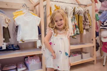 Cute little girl on shopping chooses summer clothes.