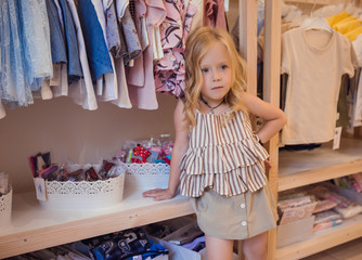 Cute little girl on shopping chooses summer clothes.