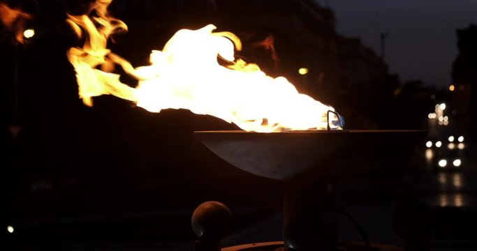 cinematic slow motion shot of fire pot torch burning with car lights in the background at night time